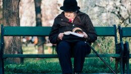 old folk reading a book sitting on a chair in the park